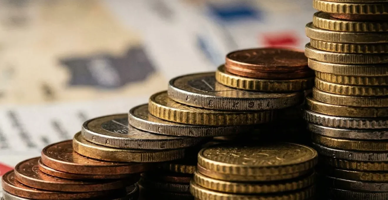 Vue macro de pièces de monnaie empilées avec factures floues en arrière-plan, symbolisant les frais cachés d'un achat immobilier.